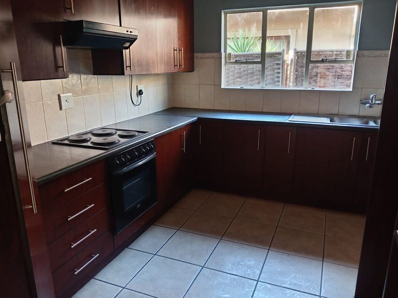 A functional kitchen featuring dark wood cabinetry, a built-in electric oven and hob, tiled splashbacks, and tiled flooring.