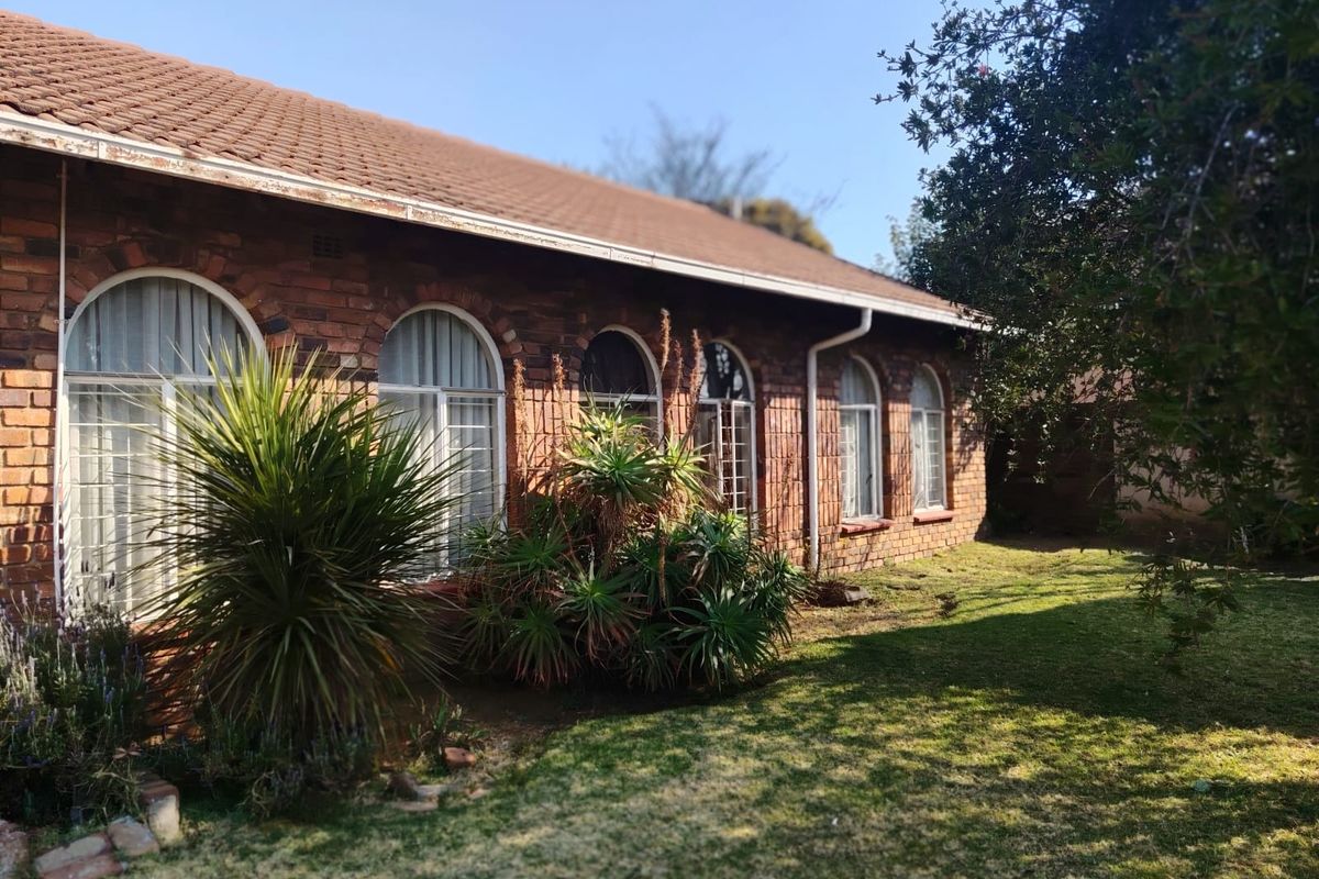 Rear view of a face brick house featuring arched windows, a tiled roof, and established garden space.