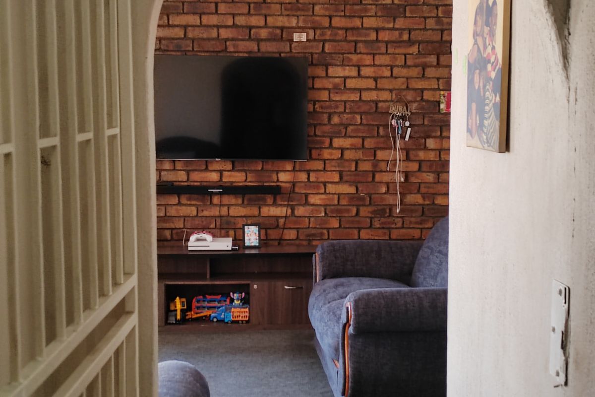 A living room featuring a prominent exposed brick wall, viewed through a security gate entrance.