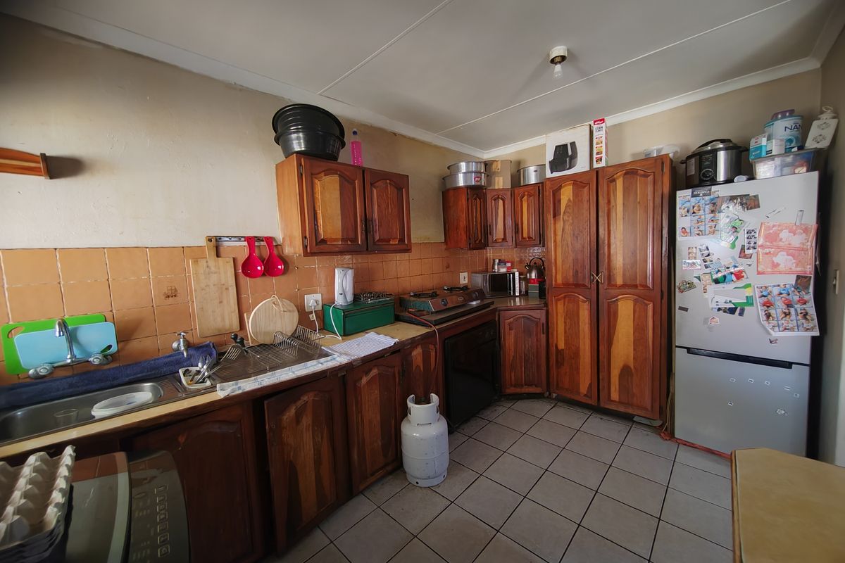 A dated kitchen featuring wooden cabinetry, tiled backsplash, and tiled flooring, offering significant potential for modernization and renovation.