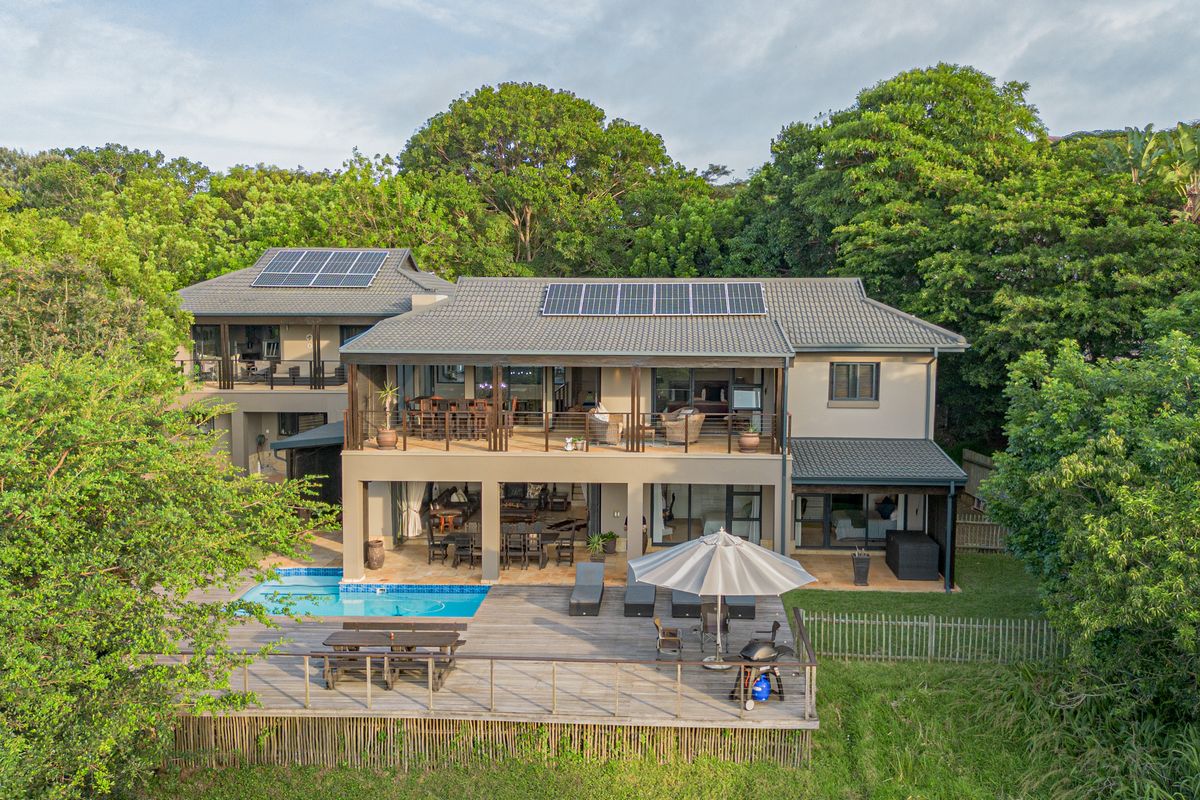 Aerial view of the rear elevation featuring a multi-level home with a swimming pool, expansive wooden deck, covered patio, and balcony.