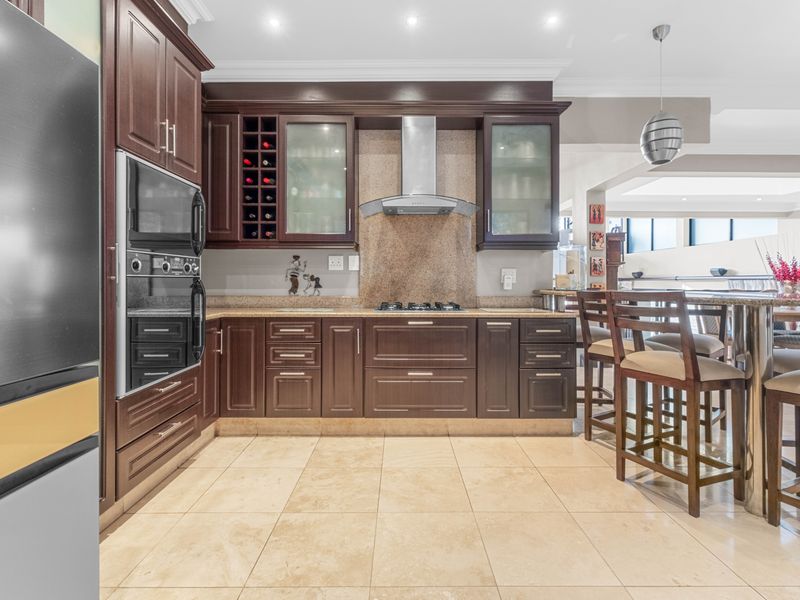 A well-appointed kitchen featuring dark wood cabinetry, stone countertops, built-in oven, gas hob, and integrated wine storage with modern recessed lighting.