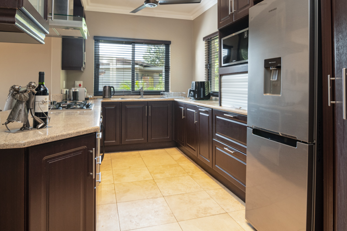A well-maintained kitchen featuring dark wood cabinetry, granite countertops, a gas hob, and built-in appliances with neutral tiled flooring.