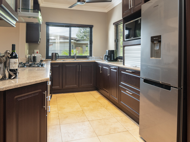 A well-maintained kitchen featuring dark wood cabinetry, granite countertops, a gas hob, and built-in appliances with neutral tiled flooring.