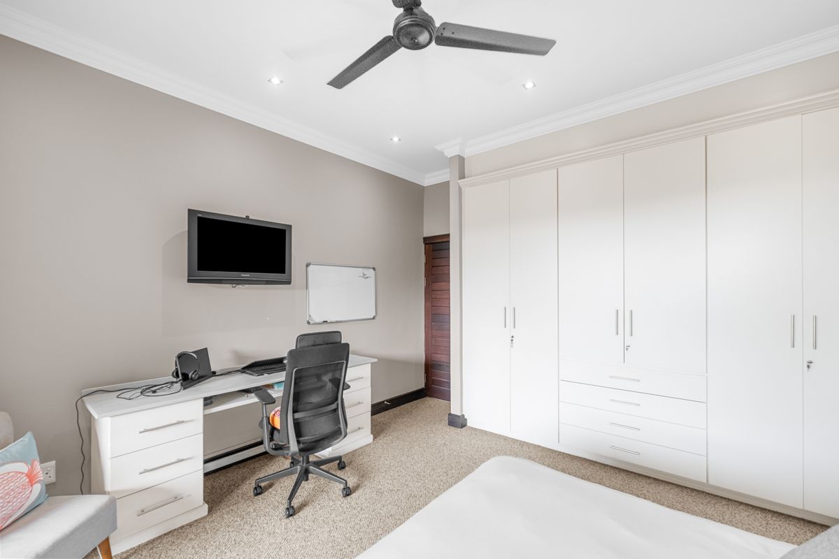 A well-maintained bedroom featuring extensive built-in cabinetry, neutral wall tones, carpeted flooring, and a ceiling fan for climate control.