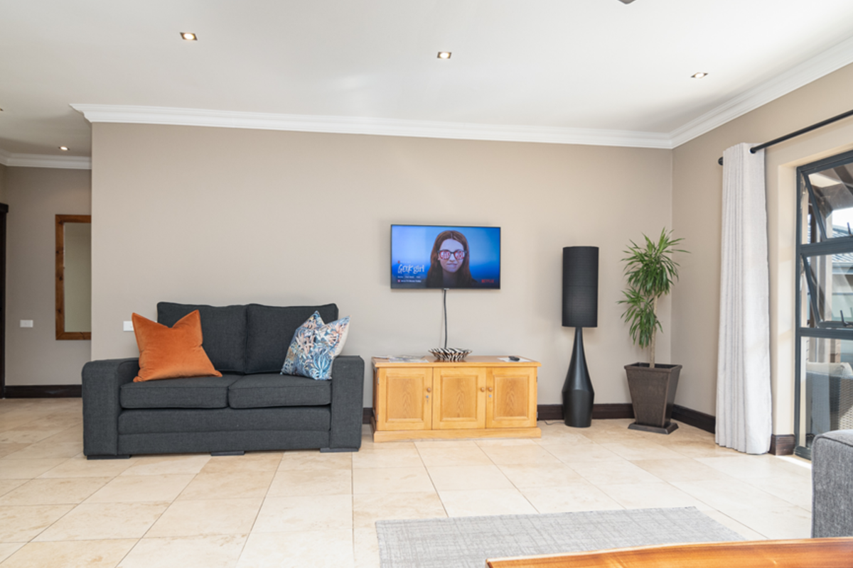 A spacious living room featuring neutral tiled flooring, recessed downlighting, decorative cornicing, and a large sliding glass door providing access to the outdoor area.