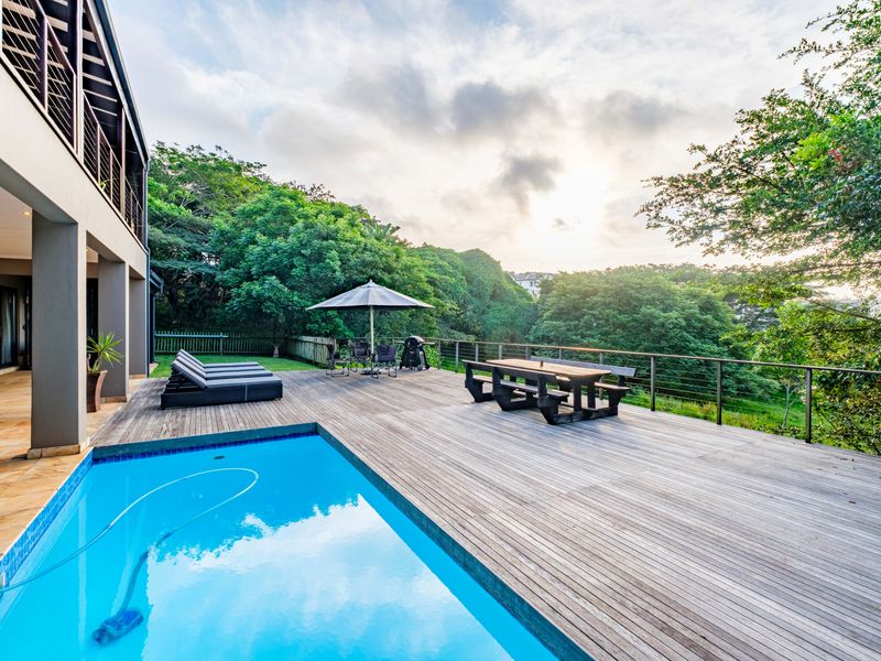 Spacious outdoor entertainment area featuring a swimming pool and extensive timber decking, overlooking a lush green landscape.
