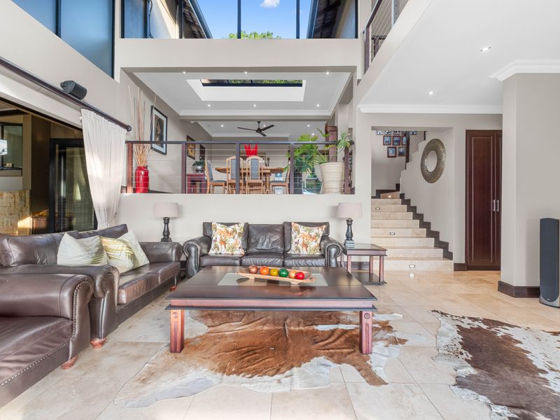 Spacious open-plan living area featuring high ceilings, a large skylight, stone flooring, and a mezzanine level with a modern staircase.