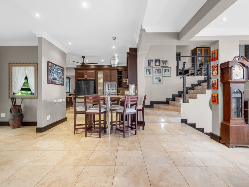 Spacious open-plan living area featuring neutral tiled flooring, recessed lighting, and a prominent staircase with modern metal railings leading to the upper level.
