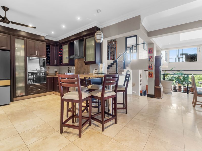 Spacious open-plan kitchen featuring dark wood cabinetry, granite countertops, and integrated appliances, seamlessly flowing into the living area with a feature staircase.