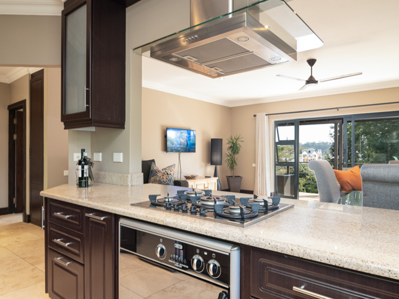 Open-plan kitchen featuring dark wood cabinetry, granite countertops, and a gas hob, flowing seamlessly into a living area with access to an outdoor balcony.