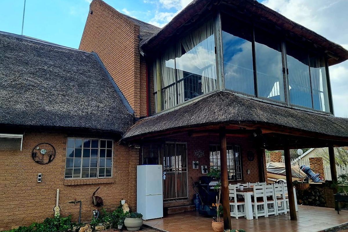 Rear view of a double-story house featuring a traditional thatch roof, brick exterior, and a spacious covered patio area with tiled flooring.