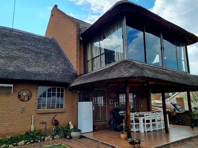 Rear view of a double-story house featuring a traditional thatch roof, brick exterior, and a spacious covered patio area with tiled flooring.