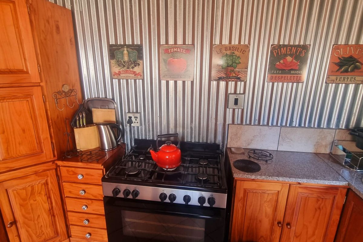 A rustic kitchen featuring wooden cabinetry, granite countertops, a gas stove with oven, and a distinctive corrugated metal splashback.