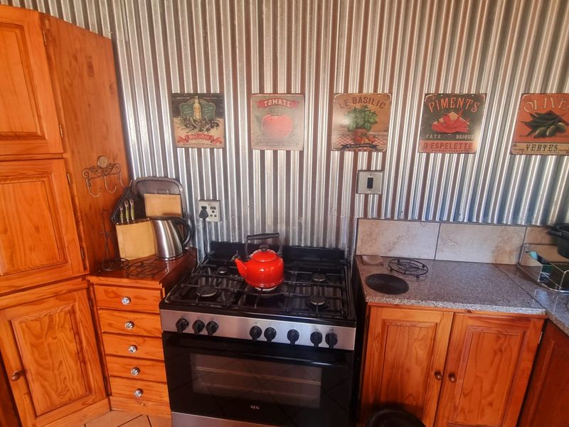 A rustic kitchen featuring wooden cabinetry, granite countertops, a gas stove with oven, and a distinctive corrugated metal splashback.