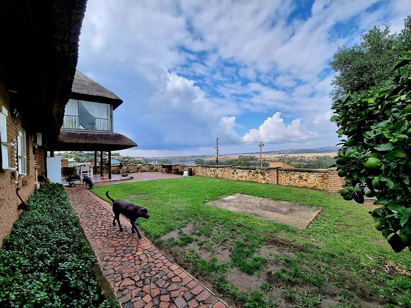 Spacious rear garden featuring a brick-paved walkway, a covered patio area, and a stone boundary wall with expansive landscape views.