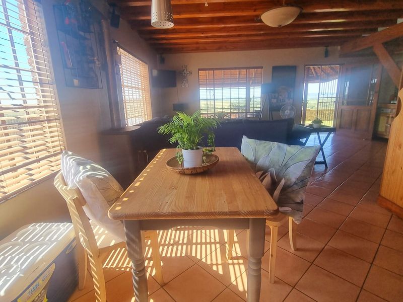 Open-plan living and dining area featuring exposed timber ceiling beams, terracotta floor tiles, and a wood-burning fireplace with natural light.