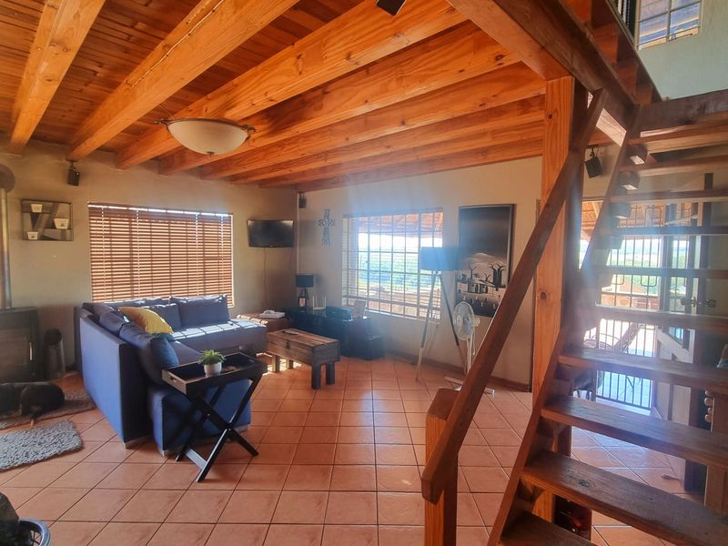 Spacious living area featuring exposed timber ceiling beams, ceramic floor tiles, and a prominent wooden staircase leading to the upper level.