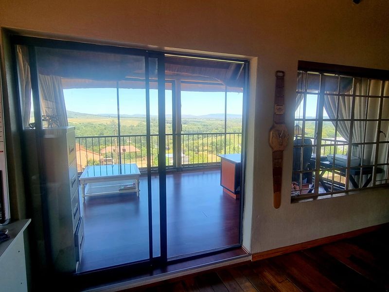 Living area featuring hardwood flooring, exposed timber ceiling beams, and large sliding glass doors opening onto a covered balcony with scenic landscape views.