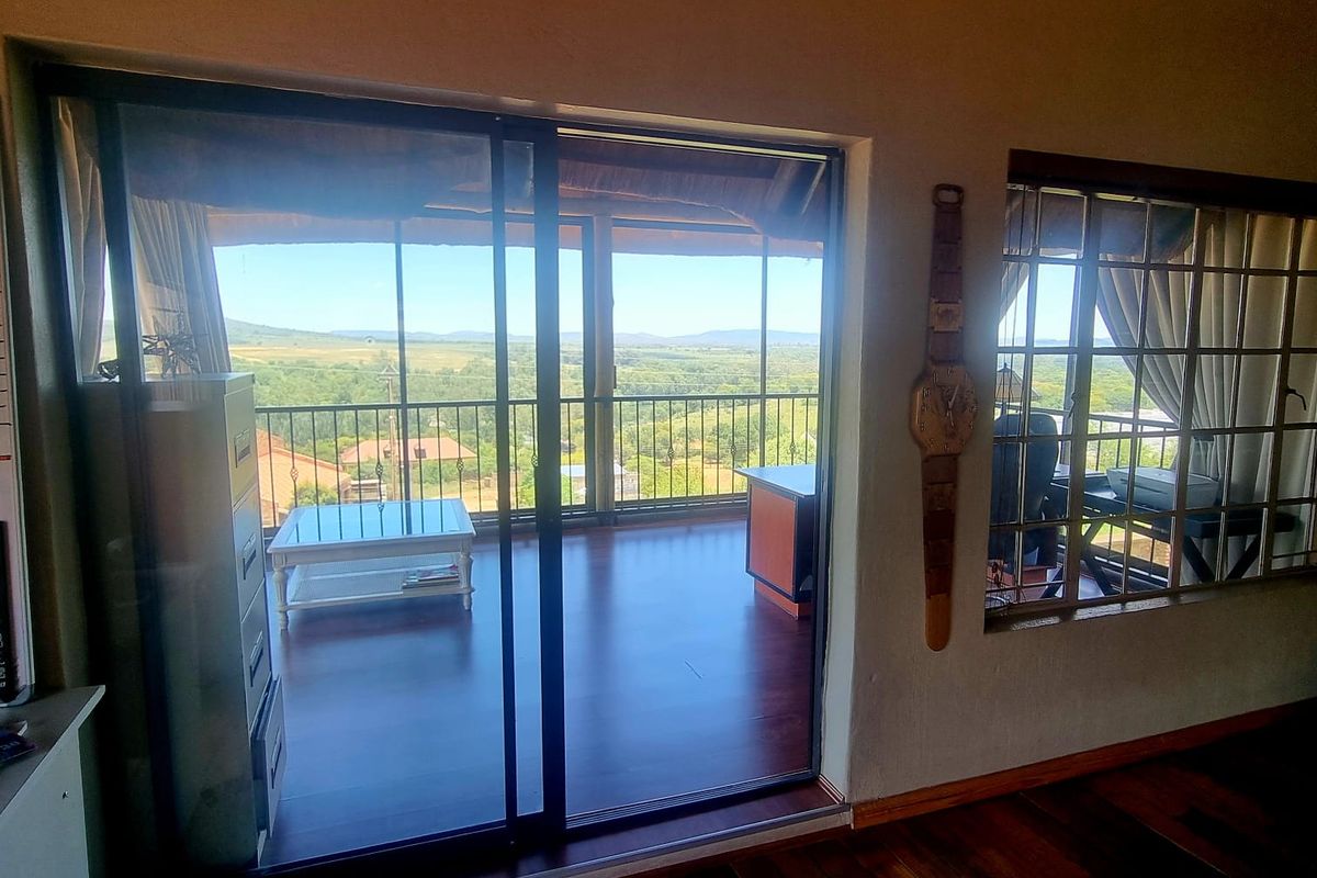 Living area featuring hardwood flooring, exposed timber ceiling beams, and large sliding glass doors opening onto a covered balcony with scenic landscape views.