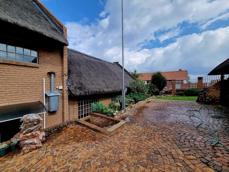 Rear exterior view of a brick house featuring a traditional thatched roof and extensive cobblestone paving in the courtyard area.