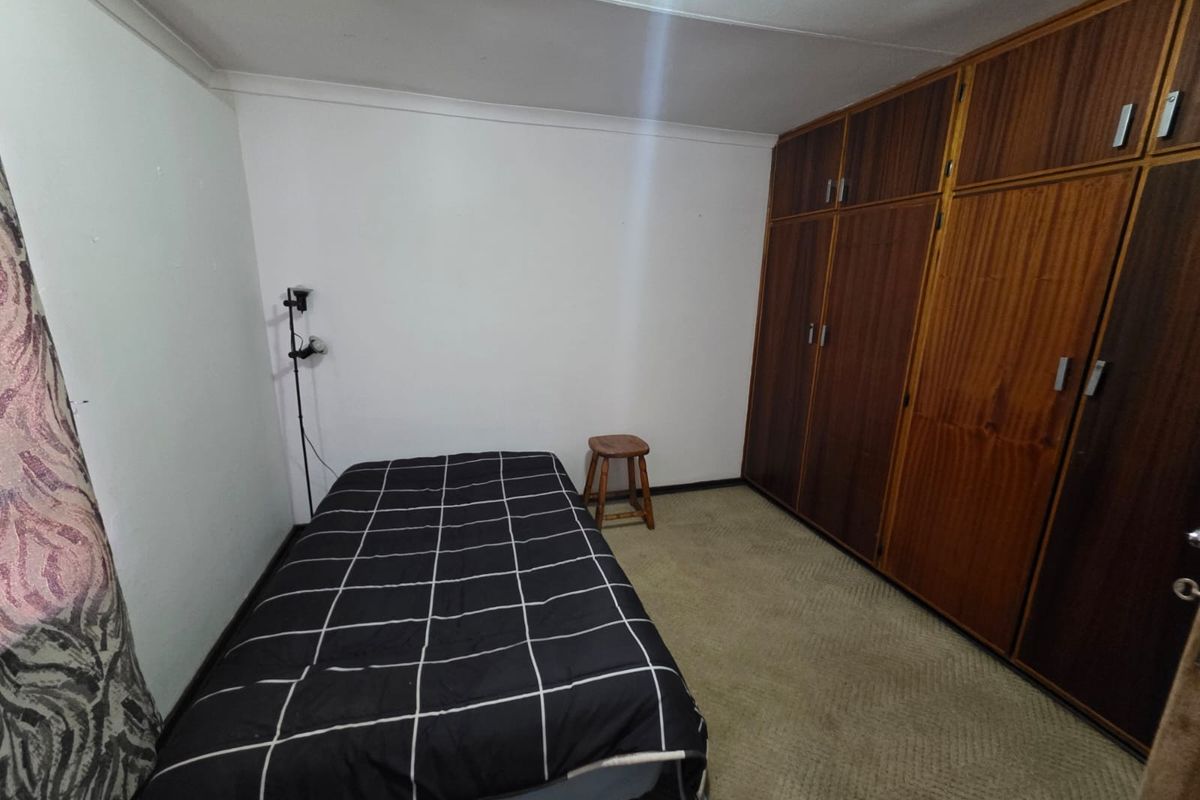 A bedroom featuring built-in wooden cupboards and carpeted flooring, offering a functional space with potential for modernization.