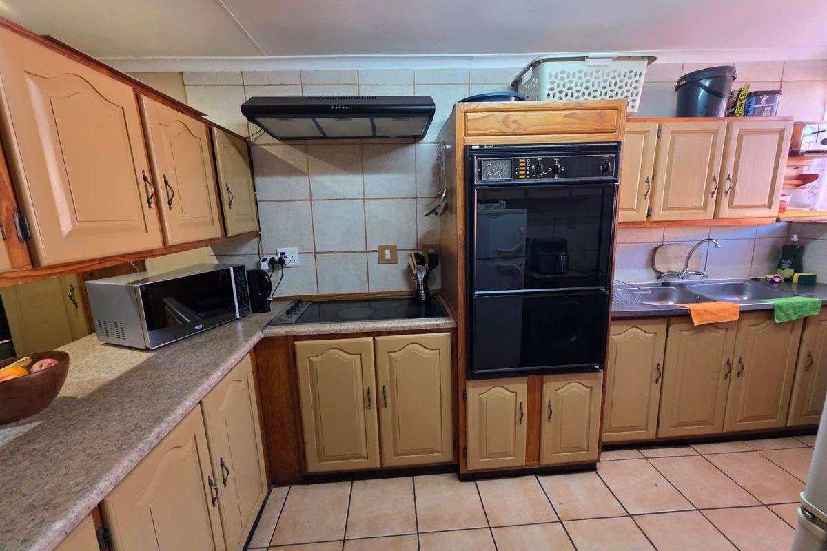 A functional kitchen featuring dated laminate cabinetry, built-in oven, electric hob, extractor fan, and tiled flooring with a double bowl stainless steel sink.