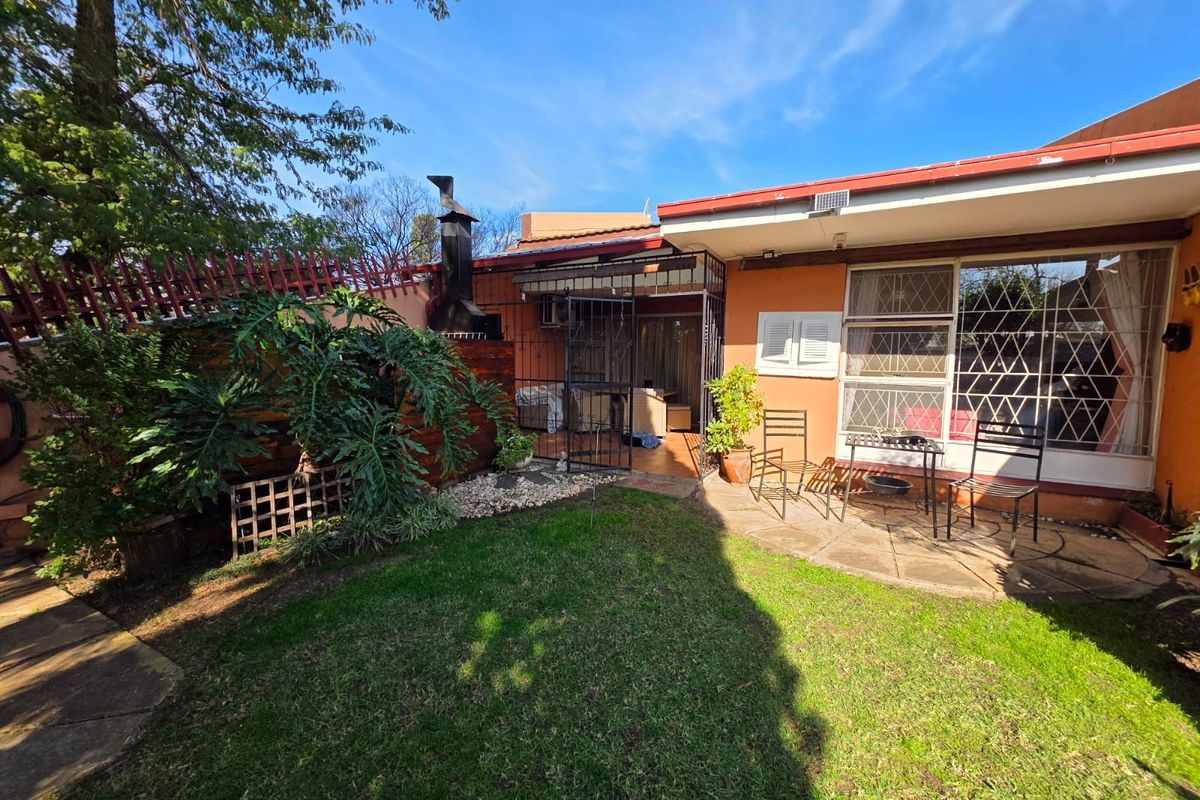 Rear garden area featuring a paved patio, built-in braai, and secure perimeter fencing with established greenery.