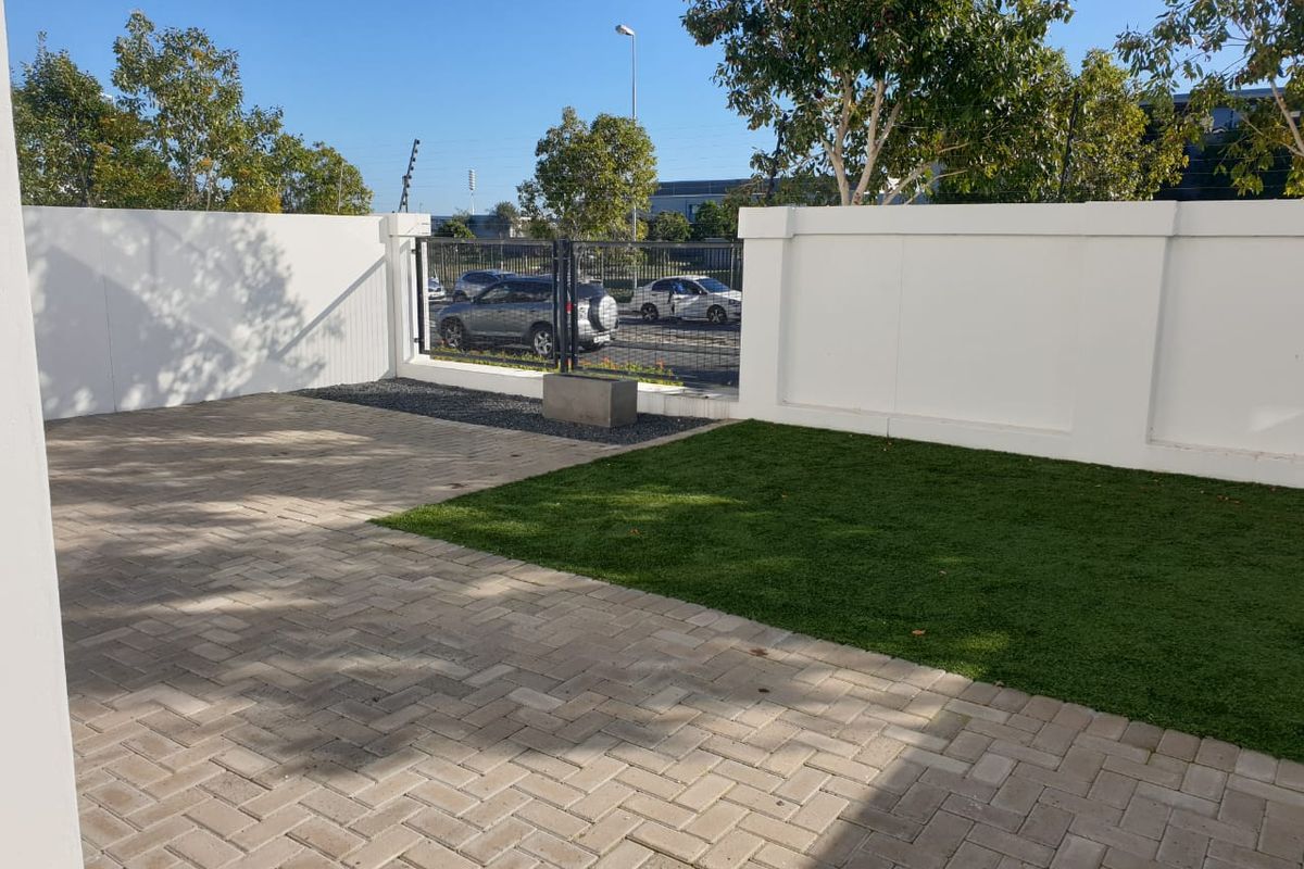 A private rear courtyard featuring paved flooring, a section of artificial lawn, and secure boundary walls with an integrated metal gate.
