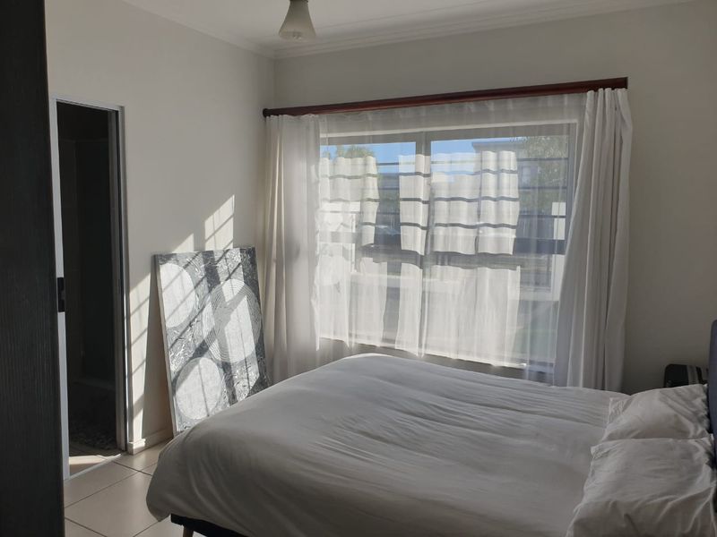 A bright bedroom featuring tiled flooring, a large window with curtain rods, and direct access to an adjoining room.