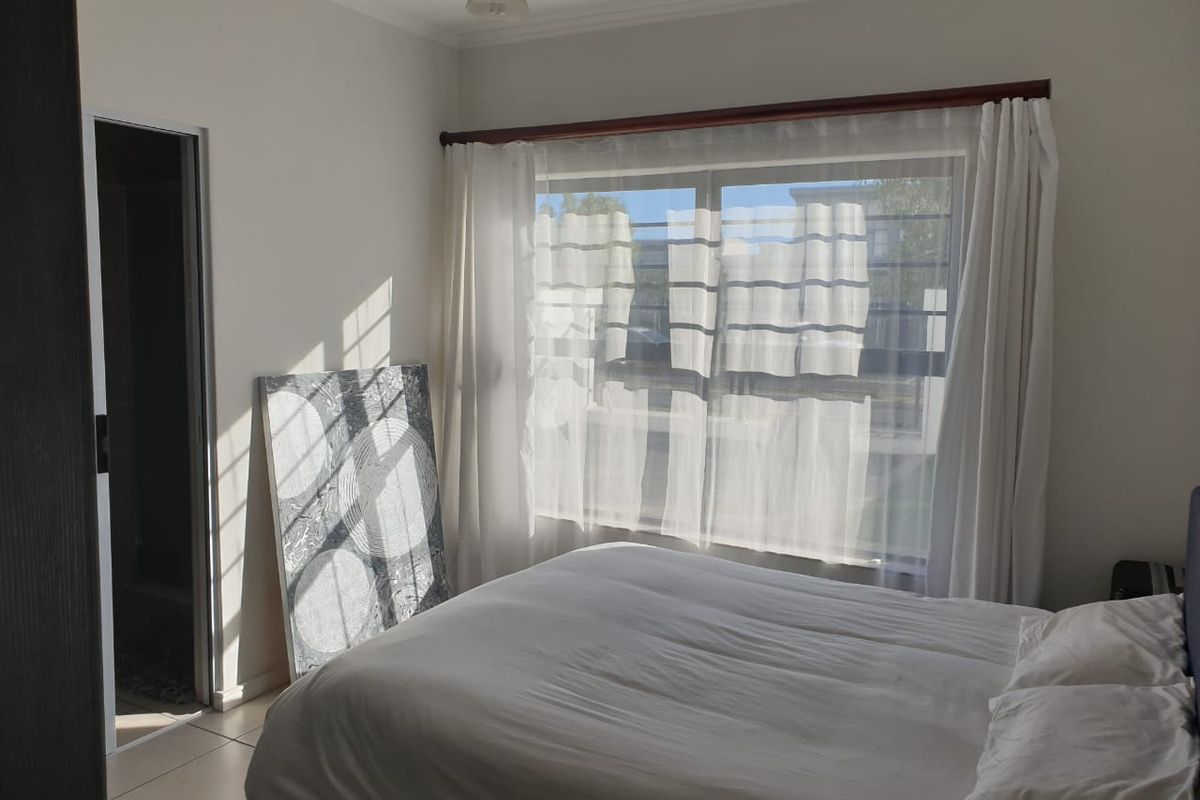 A bright bedroom featuring tiled flooring, a large window with curtain rods, and direct access to an adjoining room.