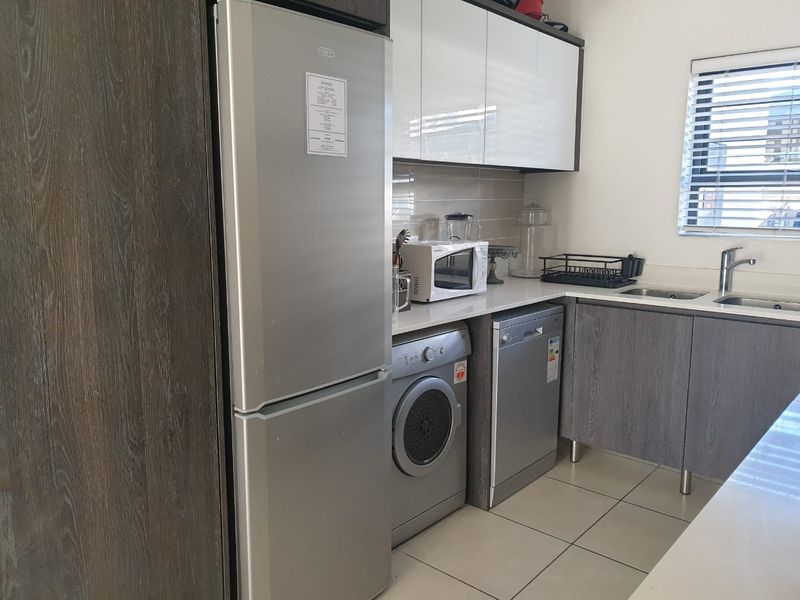 Modern kitchen featuring sleek cabinetry, tiled backsplash, integrated appliance spaces, and neutral tiled flooring with natural light from a window.