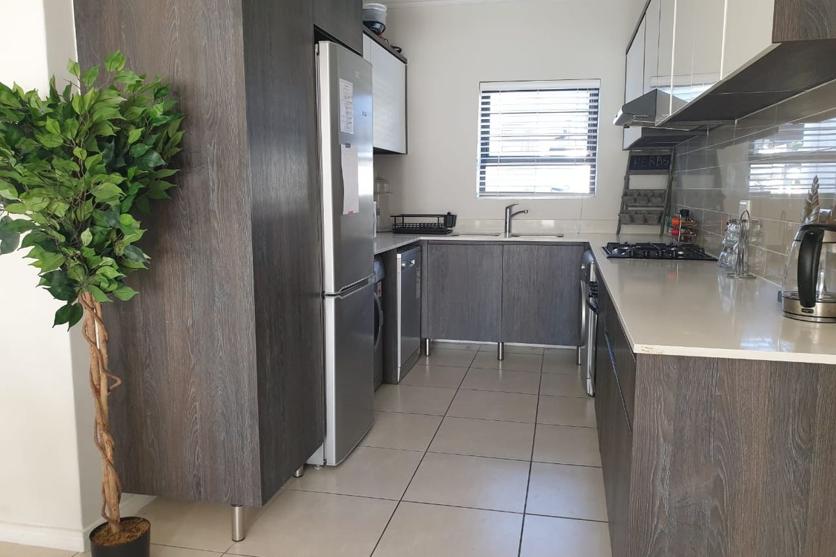 Modern kitchen featuring dark wood-grain cabinetry, stone countertops, a gas hob, extractor fan, and tiled flooring with a functional layout.