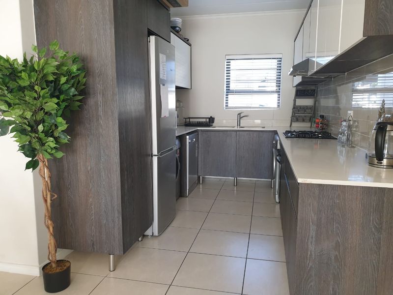 Modern kitchen featuring dark wood-grain cabinetry, stone countertops, a gas hob, extractor fan, and tiled flooring with a functional layout.