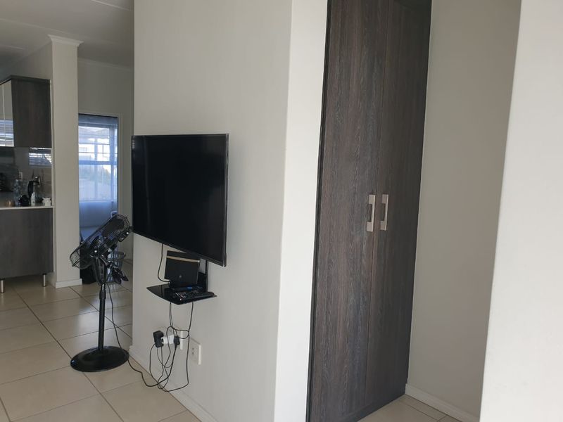 A view of a living area featuring a built-in dark wood cupboard and tiled flooring, with a wall-mounted television setup.