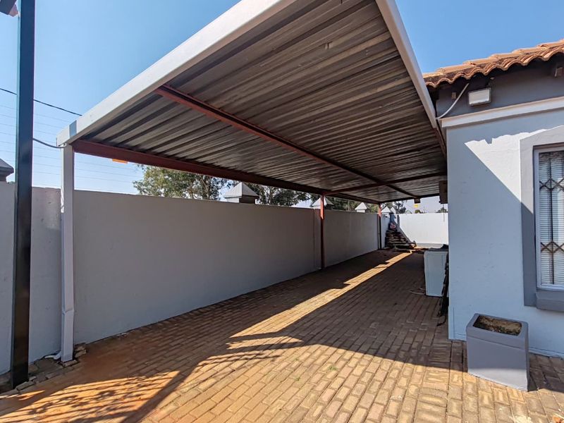 A covered carport area featuring a corrugated metal roof, steel support structure, and paved flooring, providing secure off-street parking.