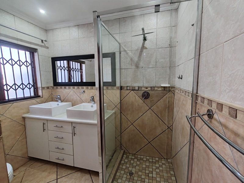 A functional bathroom featuring a double vanity with white basins, a glass-enclosed shower, and neutral-toned tiled finishes throughout.