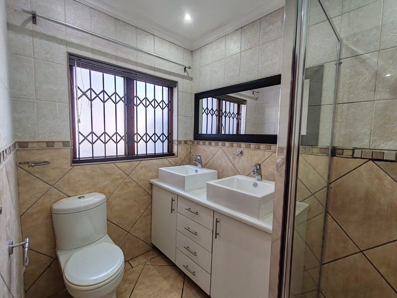 A well-maintained bathroom featuring a double vanity with vessel sinks, a shower enclosure, and neutral ceramic tiling throughout.