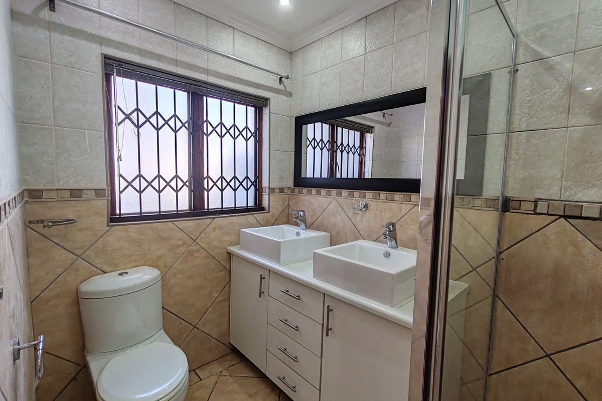 A well-maintained bathroom featuring a double vanity with vessel sinks, a shower enclosure, and neutral ceramic tiling throughout.