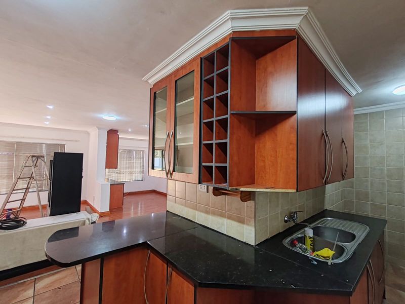 Open plan kitchen area featuring wooden cabinetry, granite countertops, and a double bowl sink, flowing into the adjacent living space.