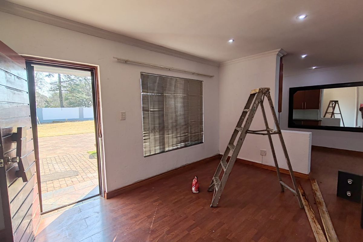 An empty living room featuring laminate flooring, recessed downlights, and a timber entrance door leading to an outdoor patio area.