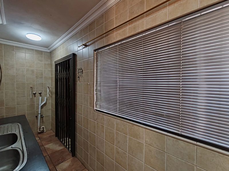 A functional laundry area featuring tiled walls and flooring, a double stainless steel sink, and a secure metal gate.
