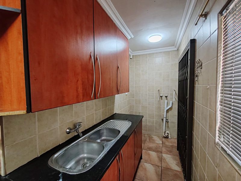 A functional laundry area featuring built-in cabinetry, a double stainless steel sink, tiled finishes, and dedicated plumbing connections for appliances.