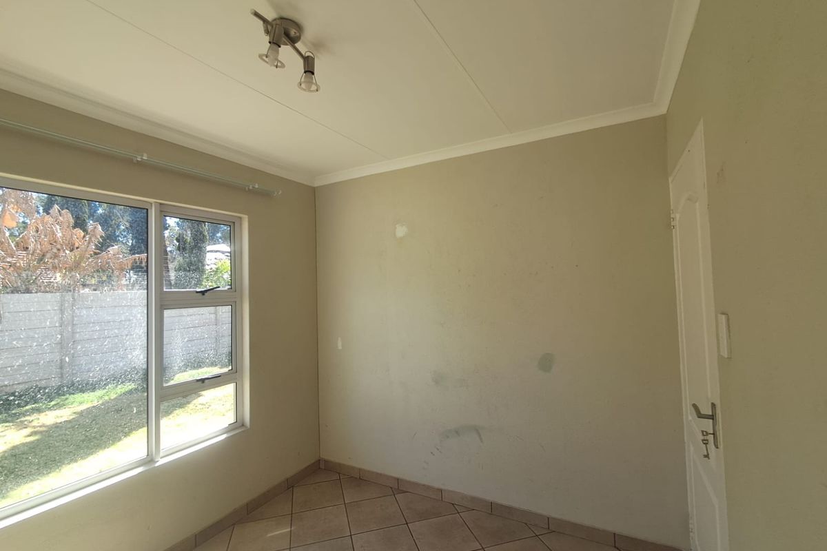 An empty bedroom featuring tiled flooring, aluminium window frames, and a ceiling light fixture, requiring minor cosmetic wall repairs and fresh paint.