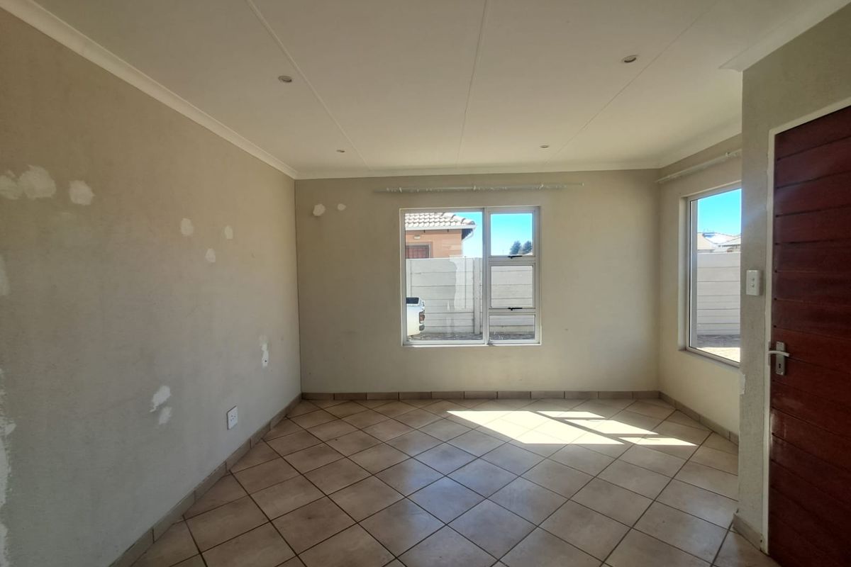 An empty living room featuring tiled flooring, recessed downlights, and aluminium windows, currently requiring wall surface preparation and painting.