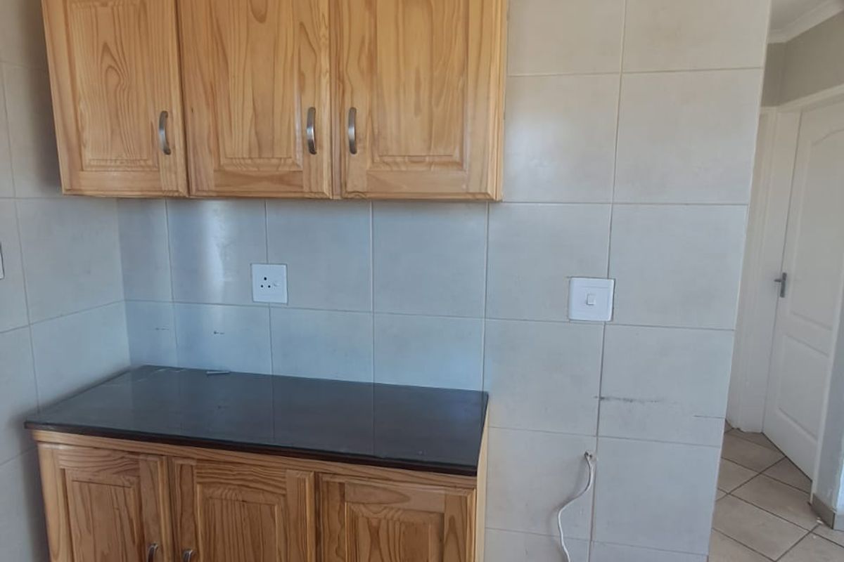 A kitchen area featuring wooden cabinetry, dark countertops, and tiled finishes, currently vacant with exposed electrical wiring.