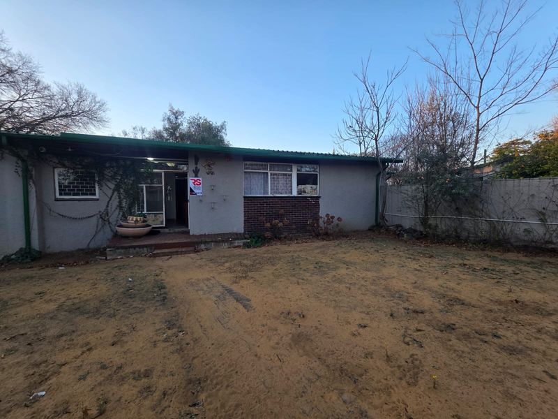 Rear view of the property featuring a plastered brick facade, metal roofing, and a large backyard area with established trees and security features.
