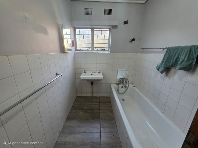 A dated bathroom featuring a built-in bathtub, wall-mounted basin, and tiled finishes, requiring cosmetic updates and repairs to wall fixtures.