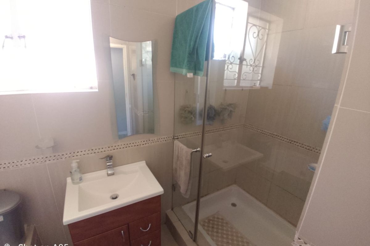 A functional bathroom featuring a vanity cabinet with a basin, a glass-enclosed shower, and neutral wall tiling.