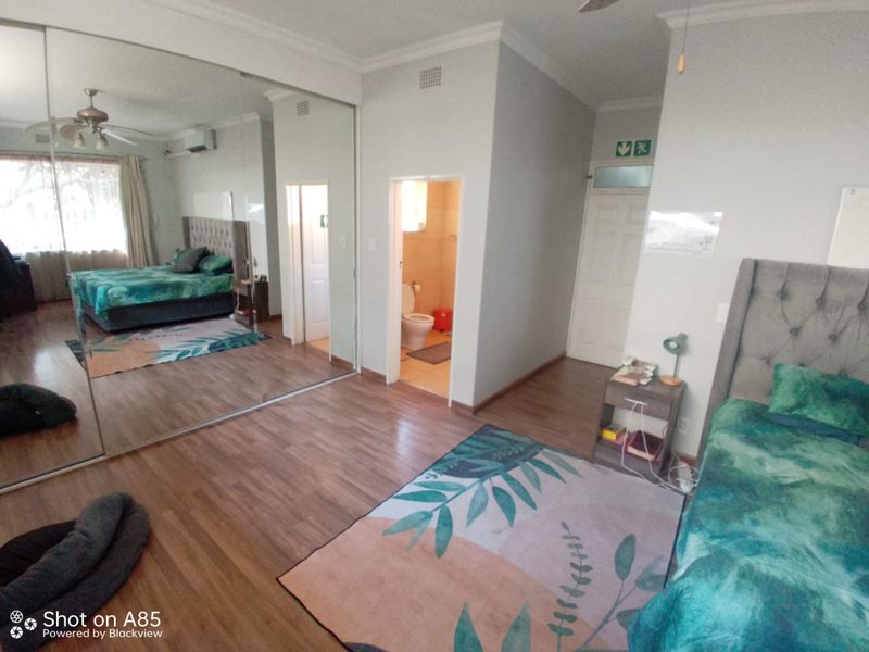Spacious bedroom featuring laminate flooring, large mirrored sliding wardrobes, an en-suite bathroom, and an integrated air conditioning unit.